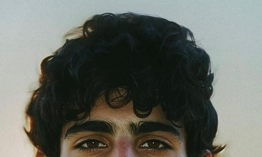 Close crop of a man's dark curly hair, from the eyes up
